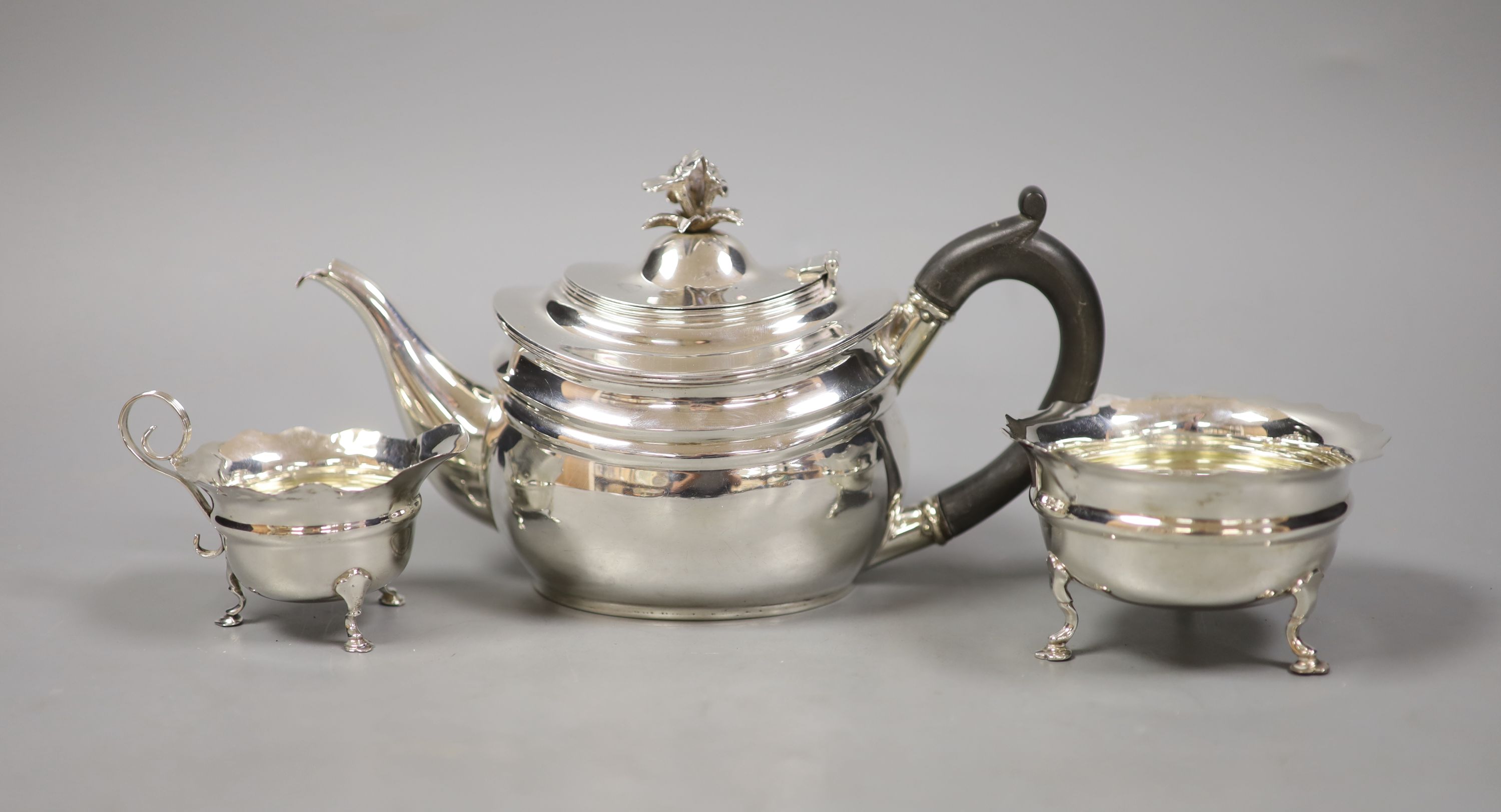A George V silver teapot with floral finial, London, 1927 together with an associated cream jug, Chester 1907 and an Art Deco silver small dish